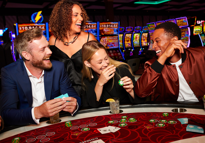 4 people at card table laughing, playing and having drinks