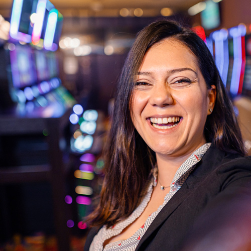A woman smiling in front of a slot machine, celebrating her Casino career.