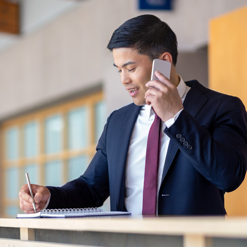 A career-driven man in a suit multitasking as he talks on the phone and holds a notebook.