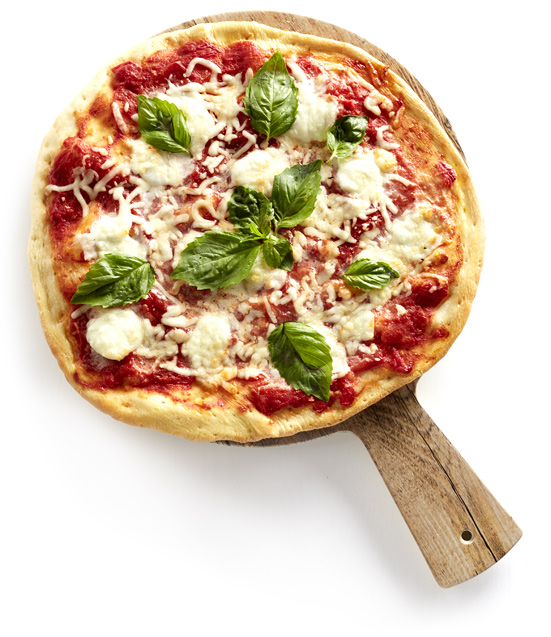 A pizza on a wooden board with basil leaves and river rock.