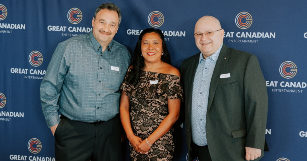 Three employees posing for photo with Great Canadian Entertainment logo backdrop