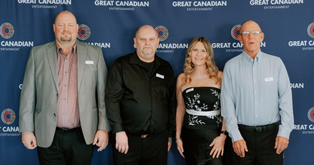 Four employees posing for photo with Great Canadian Entertainment logo backdrop