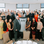 Standing Ovation Award winners and attendees standing for photo in front of River Rock stand